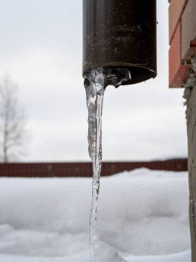 Icicle sticking out of the drainpipe. After a heavy snowstorm, the city is covered with snow and ice. There are many icicles on the facade of the building.