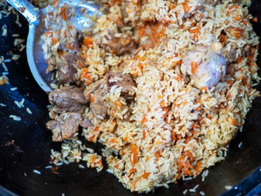 National Uzbek dish pilaf, pilaw, plov. Rice, onion, carrot and meat with a skimmer in a cauldron.