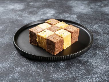 Siyah bir arka planda siyah bir tabakta duran Hint tatlıları. Hindistan tatlıları: Hindistan cevizi soan Papdi, Çikolata soan Papdi, Premium Soan Papdi, Mango Soan Papdi. Yan görünüm.