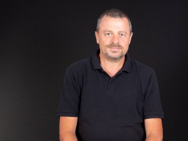 Siyah tişörtlü yakışıklı bir adam. Arka planda gülümseyen bir yüz.