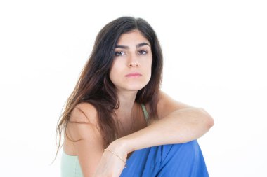 Beyaz stüdyo arka planında oturan kollarını kavuşturmuş güzel bir genç kız portresi.