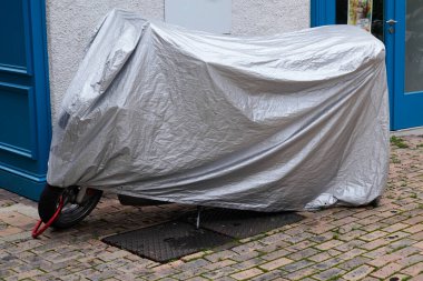 Motosiklet koruyucu plastikle korunuyor. Şehrin sokak motosikletinde branda ceketli.