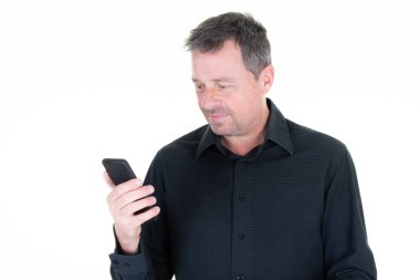 Siyah gömlekli yakışıklı adam telefonunun ekranına bakıyor.