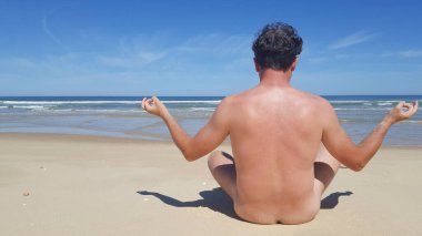 Sırtüstü çıplak doğa bilimci, boş kumsalda yoga yapıyor.