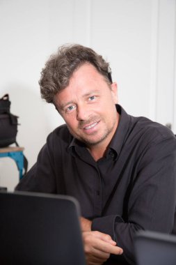 Orta yaşlı yakışıklı erkek evinin içi ofis bilgisayarında oturuyor.