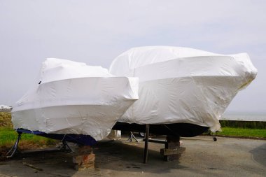 power boat parked water protected by plastic film for wintering New boats in cover casing shrink wrap on sailboat stored for winter clipart