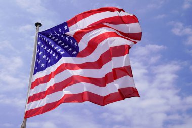 Amerikan bayrağı mavi bulutlu gökyüzünde rüzgarla minderde yüzüyor.