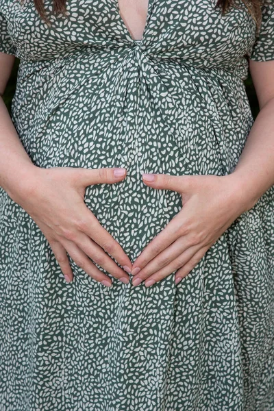 Pregnant woman tummy body in flower dress view hands make heart finger in belly pregnancy