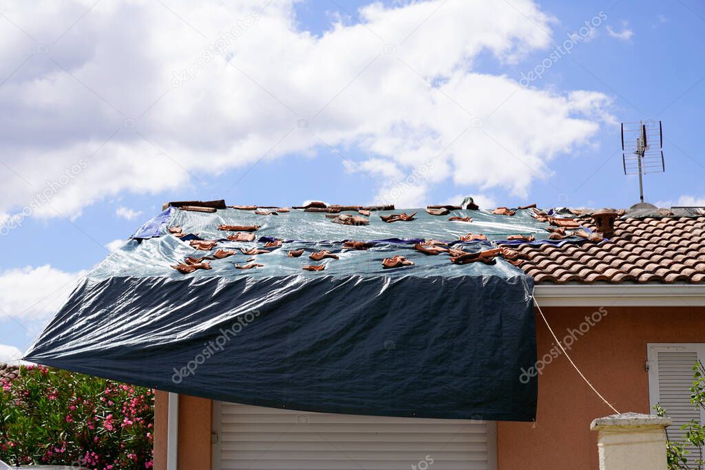 Storm damaged roof on house with a black plastic tarpaulin over hole in the shingles and rooftop after spring summer thunderstorm violent