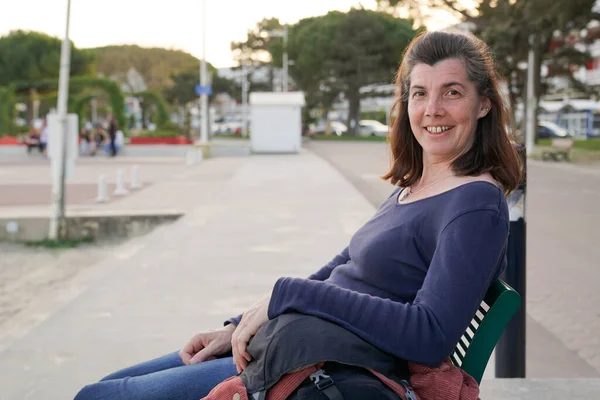 笑顔中年ブルネット女性座っているベンチで街 — ストック写真