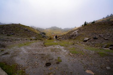 Yağmurlu bir günde dağda iki dağ arasında yürüyen yağmurluklu kişi.