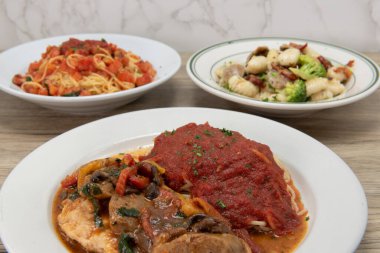 İtalyan mutfağı ziyafeti, makarna ve marinara sosuyla servis edilen mantarlı tavuk pollo Compagnola ile dolu bir yemek masası..