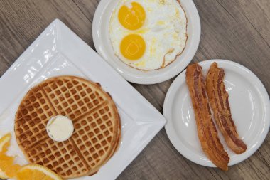 Kahvaltı menüsünün kombinasyonu; çırpılmış tereyağlı waffle, iki sahanda yumurta ve sağlıklı bir yemek için yanında domuz pastırması..