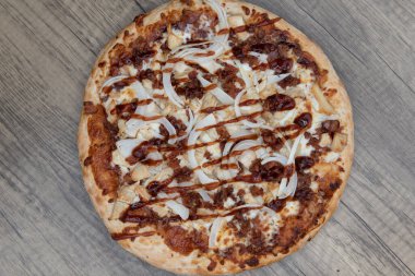 Ahşap tabakta servis edilen doğranmış et parçaları ile taze pişmiş BBQ tavuk pizzasının genel manzarası.