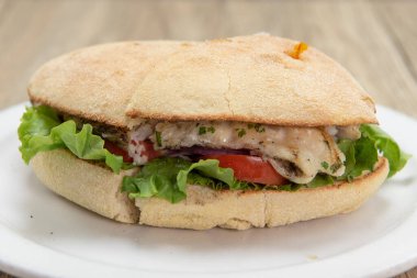 Deniz mahsullü beyaz balık sandviçi kızartılmış ve domates dilimli marul yatağında servis edilmiş..