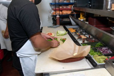 Aşçı yamağı hamburgerleri restoranın mutfak tezgahına koyuyor..