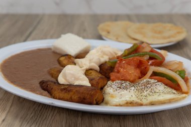 Kızarmış fasulyeli kızarmış muzlar, kızarmış sebzeler ve Latin yemeği için köpüklü ekmekle servis edilen yumurtalar..