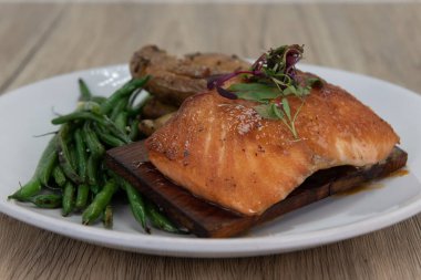 Sedir somonunun çıtır çıtır bir yüzeyle ızgara edilmiş ve yeşil fasulye ve fırında patates ile servis edilmiş sanatsal sunumu.