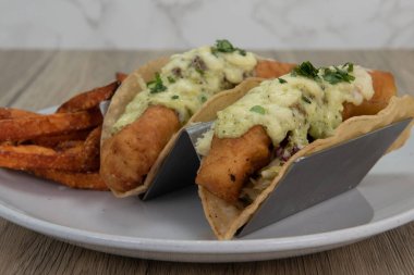 Erimiş peynirle kaplanmış ve kızarmış patates kızartmasıyla servis edilen kızarmış balıklı tacoların sanatsal sunumu..