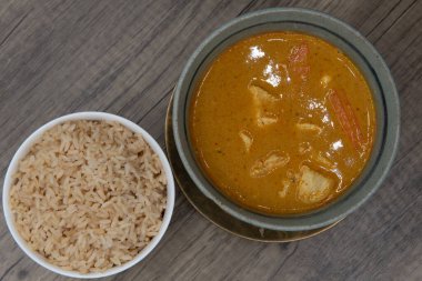 Overhead view of spicy hot bowl of yellow curry with chicken served with a side order of brown rice for a delicious Thai food meal.