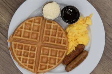 Overhead view of round waffle for tradional breakfast with sausage, eggs, syrup, and butter to fill the appetite.