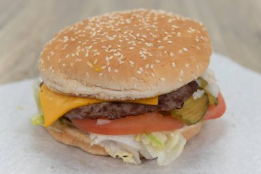 Dilimlenmiş domates, turşu ve marullu çizburgerli sandviç. Susamlı çöreğin üstünde..