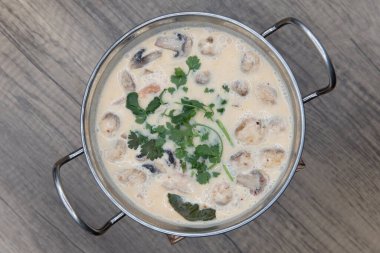 Tom Kha Kai 'nin parlak kâsesinin yukarıdan görünüşü dekoratif bir tencerede muhteşem bir yansıtıcı kapta sunuluyor..