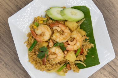 Üstünde büyük karides, bol salatalık dilimleri ve yemeye hazır ananaslı pilav tabağı var..