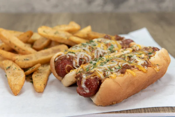 Pair of chili cheese dog hotdogs loaded with melted cheese and served with pepper steak fries for a party appetite hunger meal.
