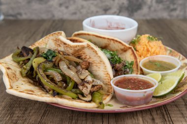 Thick homemade tortilla holds two fajita tacos loaded with stir fry vegetables, meat, cilantro and salsa dipping sauce for a fullfilling meal.