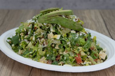 Dilimlenmiş avokado, romaine marul, peynir ve haşlanmış yumurtadan oluşan devasa salata yığınının üstünde..