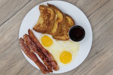 Overhead view of traditional American breakfast consisting of french toast, fried eggs, and bacon will ensure that the belly will be full.