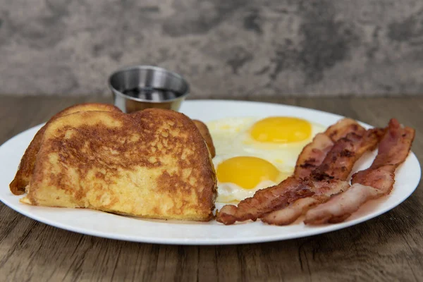 Traditional American breakfast consisting of french toast, fried eggs, and bacon will ensure that the belly will be full.