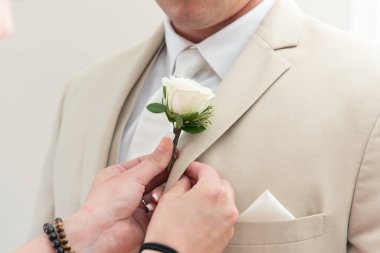 Groom has helping hands with manicure assisting him in pinning his flower rose boutonniere on the lapel of his suit.