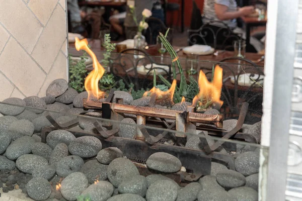 Natural gas fireplace has soothing flame buring over a bed of rocks in dining area.