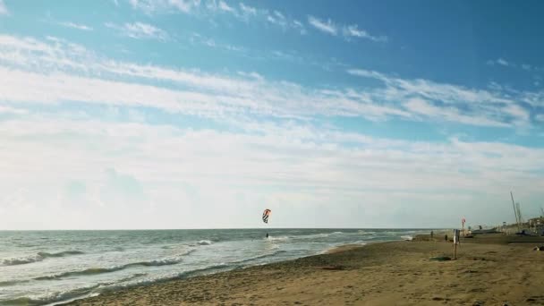 波のクレストにカイトサーファー。白い雲と青空。波の中でカイトサーファーと海の風景。カラフルなカイトサーフィン帆は曇り空を飛ぶ — ストック動画