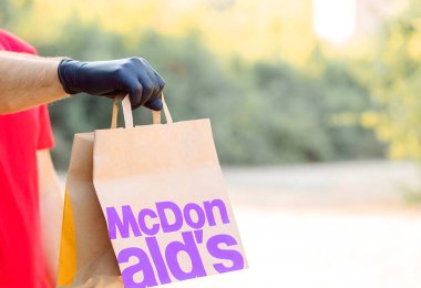 Tıbbi eldiven giymiş bir adamın elinde kağıt torba McDonals bulunur. Teslimat McCafe. Fast food restoranı McDonalds. McDonals 'ı götürün.