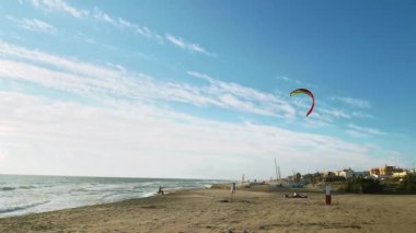 Dalganın tepesindeki uçurtmacı. Beyaz bulutlu mavi gökyüzü. Dalgalarda uçurtmacılar olan deniz pelerini. Renkli uçurtmalı yelken bulutlu gökyüzünde uçar. 