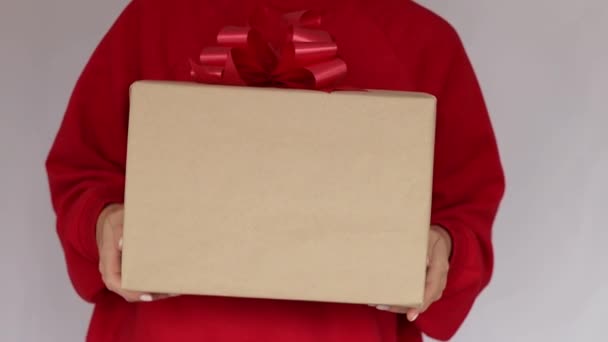 Geschenke in Frauenhänden. Expresszustellung. Eine junge Frau im roten Sweatshirt hält einen Karton mit roter Schleife in der Hand. Online-Shopping-Verkauf. Quarantäne. Online-Lieferung — Stockvideo