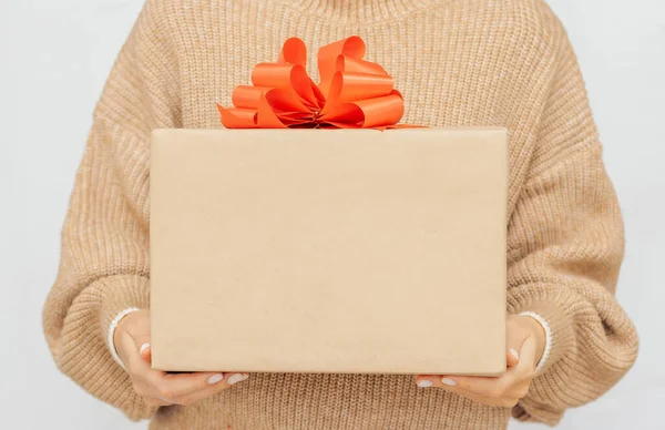 Womans hands gift box with red ribbon. woman in warm beige jumper Hold present box with bow. 
