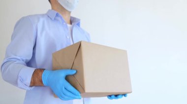 Tıbbi maske ve tıbbi eldiven içinde karton kutu taşıyan teslimatçı. Ekspres teslimat, online alışveriş. Coronavirus bağış kutusu. Yemek teslimatı. Yemek yardımı.