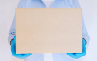 Teslimatçı, tıbbi eldivenlerin içinde karton kutu tutuyor. Ekspres teslimat, online alışveriş. Coronavirus bağış kutusu. Yemek teslimatı. Yemek yardımı.