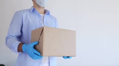 Tıbbi maske ve tıbbi eldiven içinde karton kutu taşıyan teslimatçı. Ekspres teslimat, online alışveriş. Coronavirus bağış kutusu. Yemek teslimatı. Yemek yardımı.