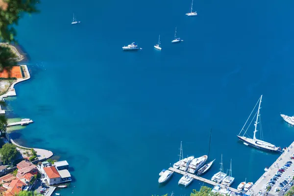 Kotor Körfezi 'ndeki limanın ve Kotor şehrindeki sahil şeridinin nefes kesici panoramik manzarası. Koyun sakin, berrak mavi suları ve kıyıya demirlemiş beyaz zevk yatları.