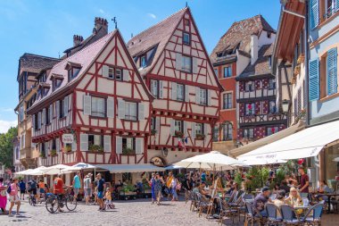 Colmar, Fransa, Ağustos 2022, İnsanlar Alsace, Colmar 'daki geleneksel peri evlerinin renkli yüzleriyle eski kasaba meydanındaki bir yazlık kafede dinleniyor.