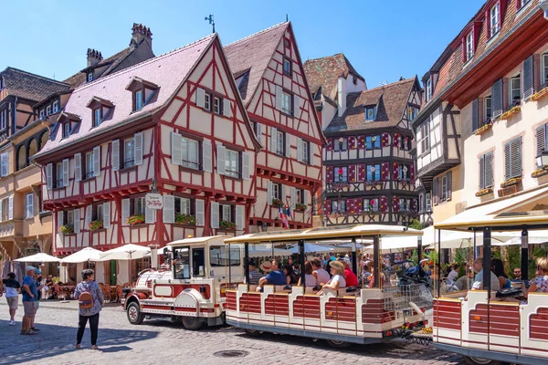 Colmar, Fransa, Ağustos 2022, insanlar kırmızı bir turist treniyle Colmar, Alsace 'deki geleneksel peri evlerinin parlak renkli cephelerine bakarak şehri geziyorlar.