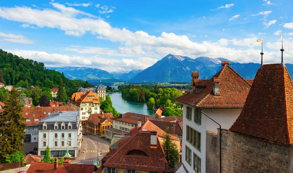 Eski Thun kasabasındaki kilisenin panoramik manzarası, binaların kiremitli çatıları, göl ve arka plandaki dağlar.
