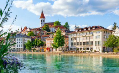 İsviçre 'nin Thun kentinin seddi, çiçekler ve ağaçlarla süslenmiş antik mimarisinin panoramik görüntüsü şeffaf gök mavisi nehrine yansımaktadır.