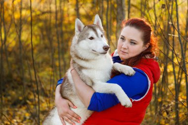 Köpek yetiştiricisi güz ormanında köpeğine sarılıyor.
