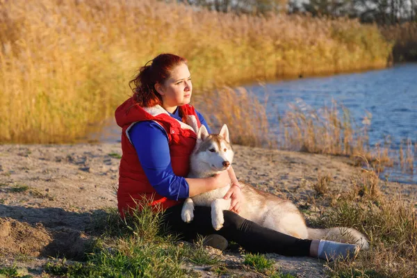 犬の飼育員は湖の海岸で犬と抱き合っている — ストック写真